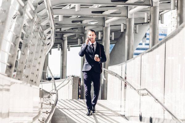 Portrait of handsome businessman in black suit standing and using smartphone outdoors on modern city background.man working with technology devices concept