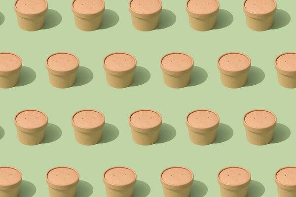 Pattern made with brown disposable kraft paper street food or ice cream containers with paper caps over light green background, mockup image. Sustainable street food packaging concept