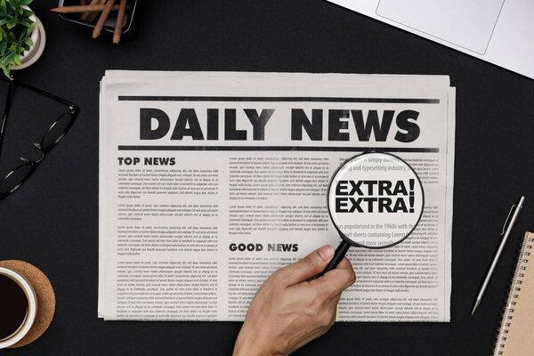 Hand using Magnifying glass at  Business Newspaper and office supplies with notebook, hot coffee cup, glasses, books and accessories on black desk topview, Daily Newspaper mockup concept