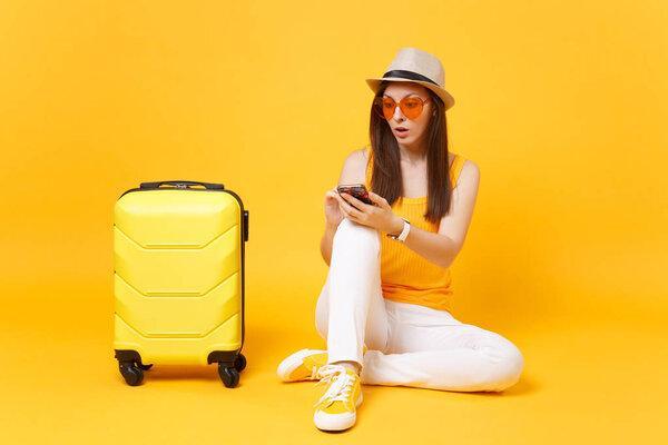 Tourist woman in summer clothes, hat with mobile phone with friend, booking taxi, hotel isolated on yellow orange background. Passenger traveling abroad to travel weekends getaway. Air flight concept