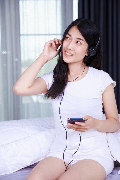 woman in headphones listening to music from smartphone on bed in