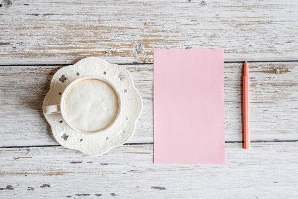 Morning coffee mug for breakfast, pink paper blank on white wooden table, top view, flat lay style. Woman working desk. Mockup, overhead
