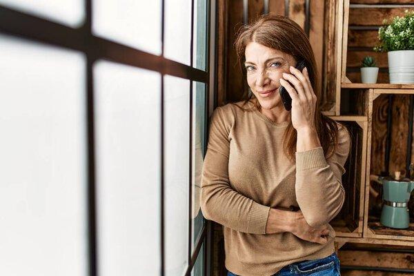 Middle age caucasian woman talking on the smartphone standing at home.