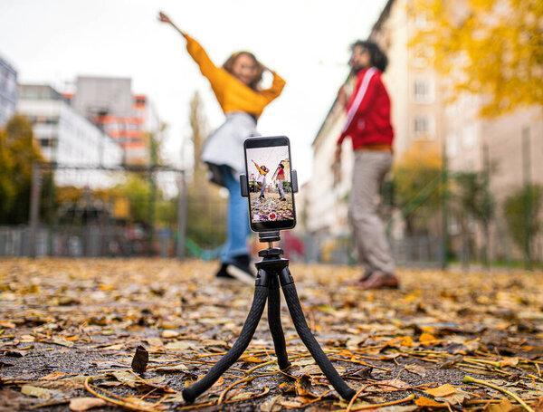Young couple with smartphone making video for social media outdoors in park.