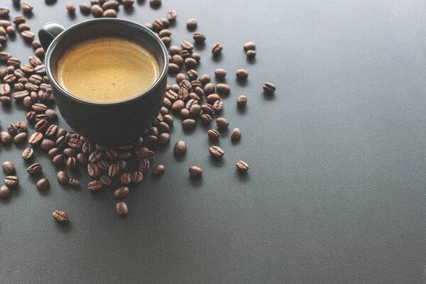 hot espresso and coffee bean on black table with soft-focus and over light in the background. top view and vintage color tone