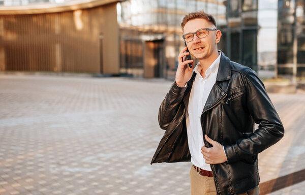 Handsome man with glasses with a smartphone on the street of a big city. Businessman talking on the phone on urban background