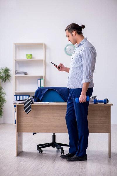 Young handsome male employee doing exercises in the office