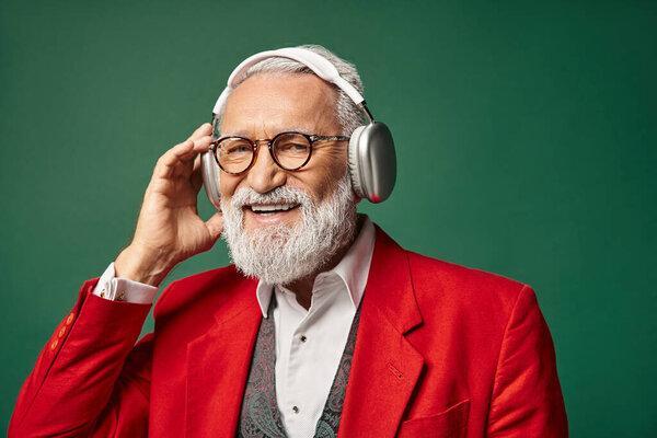 good looking elegant man in red Santa suit wearing headphones and smiling at camera, winter concept