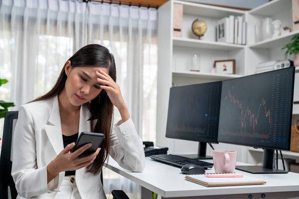 紧张的年轻漂亮的亚洲女商人专注于智能手机，在现代办公室的掌上电脑显示屏上分析可能的盈利或亏损风险。Stratagem.