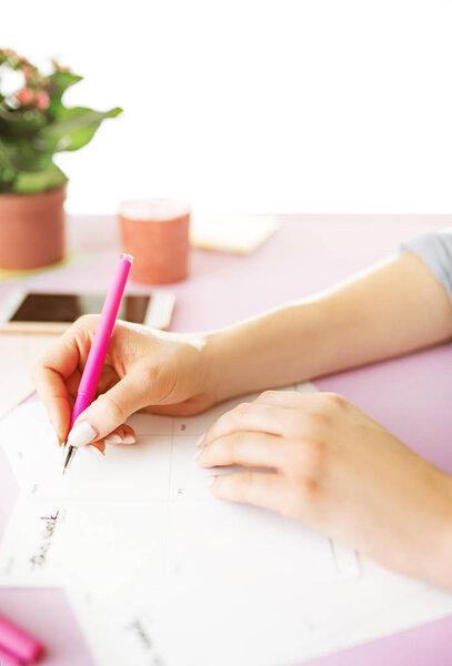 The female hands holding pen. The phone on trendy pink desk.