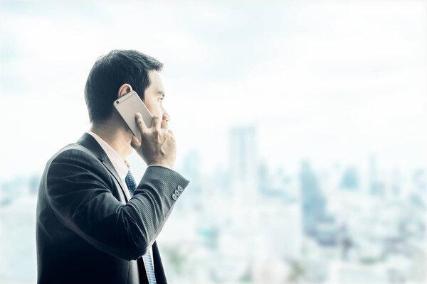 Businessman using mobile phone looking through office window to 