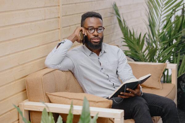 African American in an office or coworking talking on the phone and taking notes in a notebook 