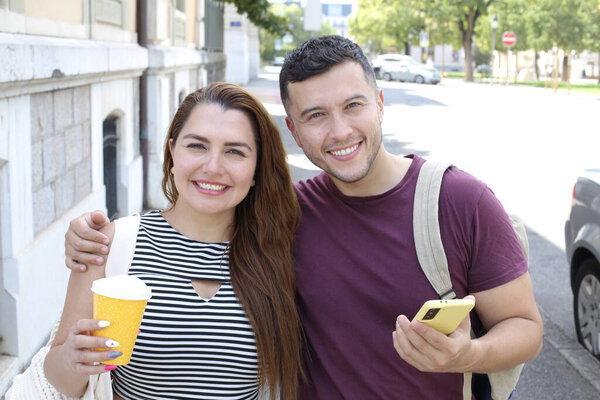 portrait of young happy couple with paper cup of coffee and smartphone on city street together