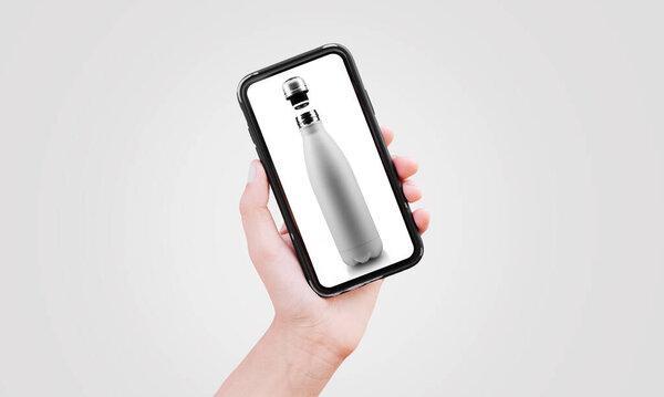 Smartphone in hand with thermo water bottle on screen. Grey background.