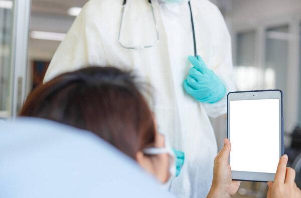 Asian female patients wear patient gown in the detention center using tablet for video call. Mockup and social distance concept.