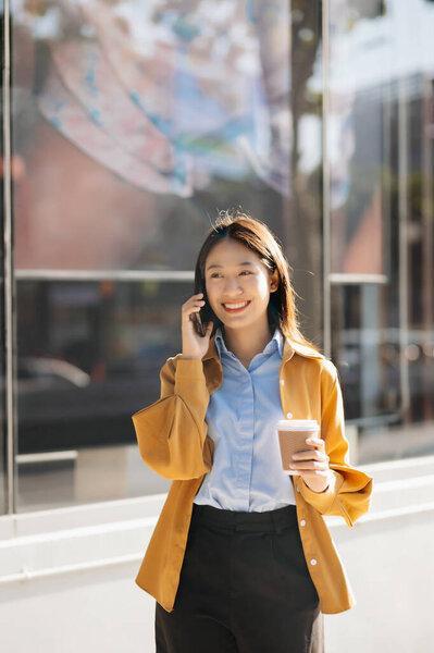 Young Asian businesswoman using smartphone on the street in big city with business center on the background 