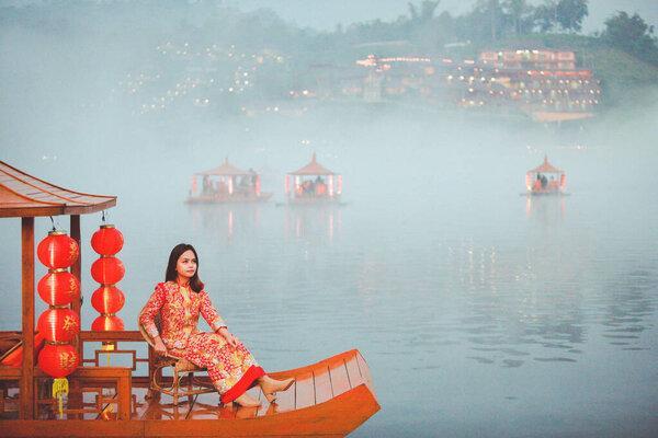Beautiful Asian Chinese Woman Wearing Cheongsam Traditional Red Dress on Chinese New Year travel on vacation Posting on a boat in the river. 