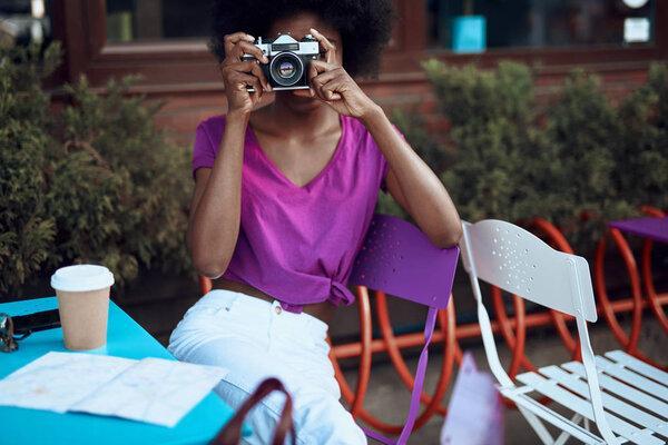 Young afro-american lady is using retro camera in cafe