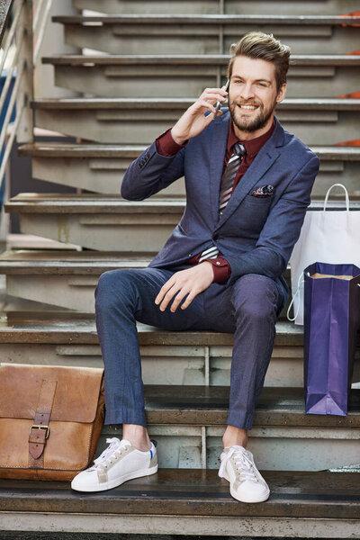 I never come back empty handed. a well dressed young man using his phone on a shopping spree
