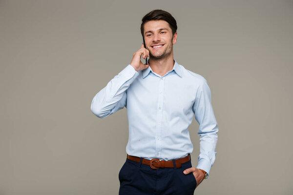 Image of happy handsome man wearing formal clothes smiling and talking on cellphone