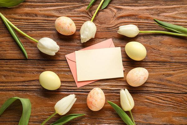Beautiful Easter composition with blank card, painted eggs and flowers on wooden background