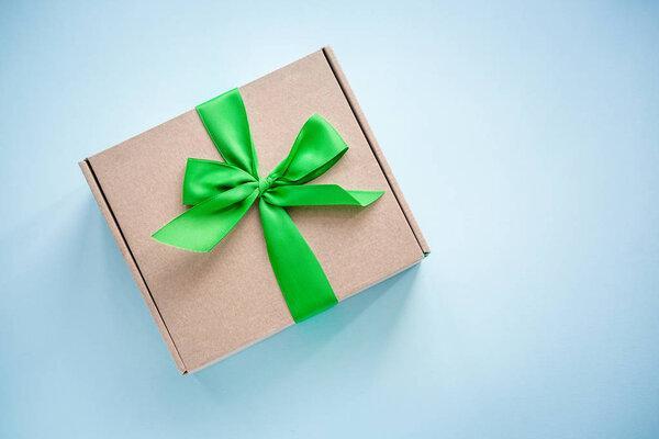 One craft paper box  with green ribbon bow on blue background from above. Minimalism, copy space
