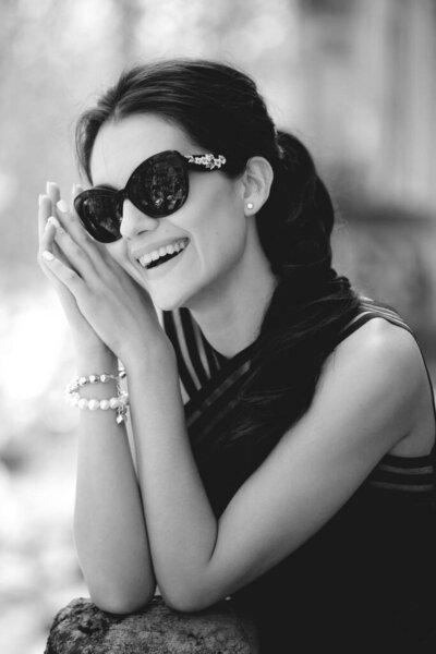 Cheerful stylish woman with sublime body, wearing in a elegant black dress and sunglass, in daytime posing on balcony.