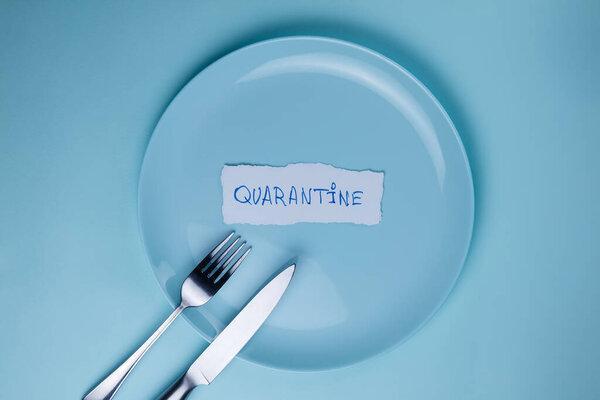 The inscription Quarantine on an empty blue plate with a fork and knife on a blue background