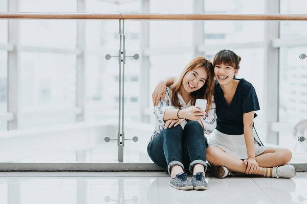  Asian girls best friends laugh and smile while having fun with smart phone