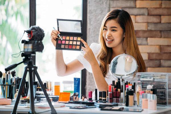 Charming Asian girl recording vlog. Beauty blogger presenting makeup cosmetics in front of camera