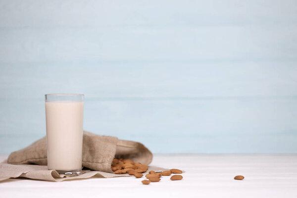 Glass of almond milk with almond nuts on canvas fabric on white wooden table. Dairy alternative milk for detox, healthy eating and diets. Selective focus