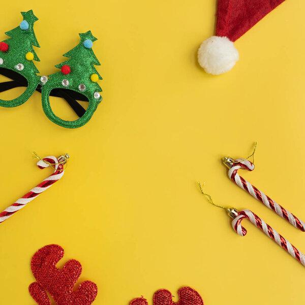 Funny New Year, Christmas accessories for winter holidays party celebration on yellow background with blank copy space. Christmas eyeglasses, candy canes, deer horns, Santa hat, toy trees