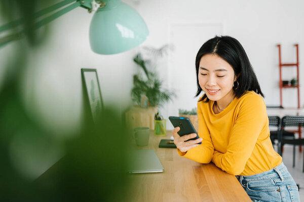 Young asian woman using mobile phone while relaxing on workplace at home