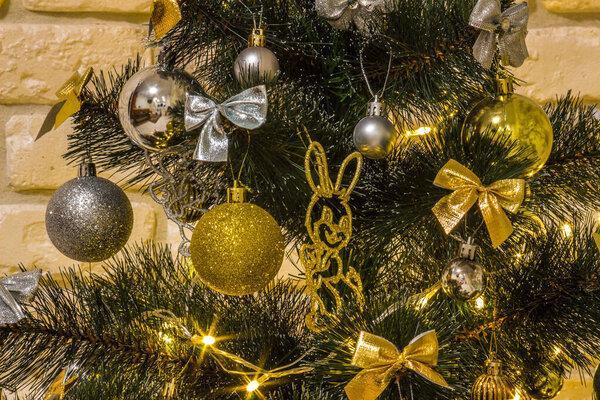 Christmas composition in the evening illumination of lighted garlands. Xmas fir tree with baubles, multi-colored bows, animals, bells, glowing lights. Holidays concept. Close-up with selective focus