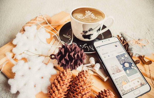 Cup of coffee and phone on a wood tray with christmas decorations and cones