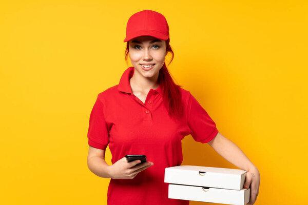 Pizza delivery girl holding a pizza over isolated background sending a message with the mobile