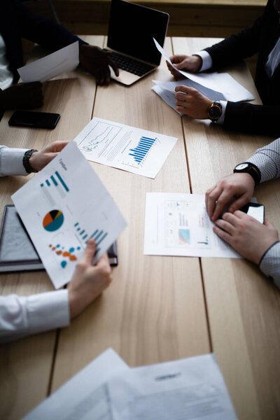 Hands of four businessmen of different nationalities with charts of company subsidiaries
