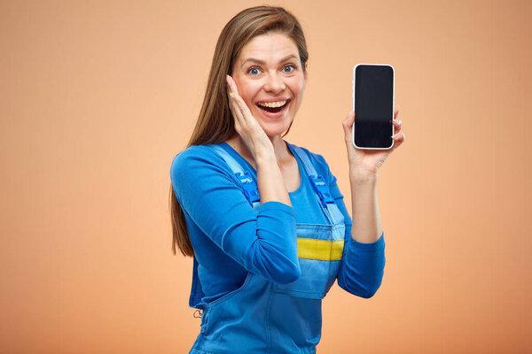 Surprising woman in overalls using smartphone. Isolated female worker portrait.