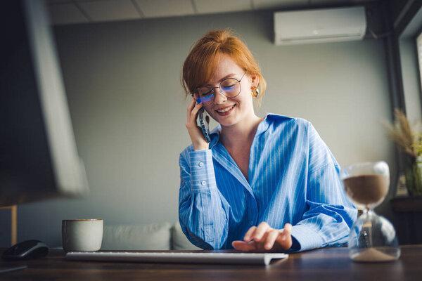 Beautiful young businesswoman having business call in office, her workplace, writing down some information.