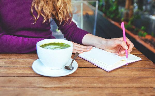 Woman's hands writting in notebook, in city cafe. Blogger's lifestyle? Tea matcha.