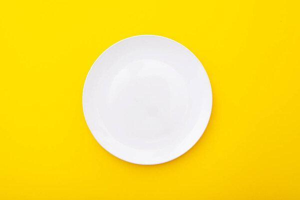 Ceramic white plate on yellow surface, kitchen table, lay out, top view, space for text