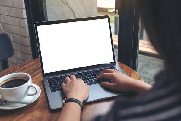 Mockup image of a woman using and typing on laptop with blank white desktop screen on wooden table in cafe