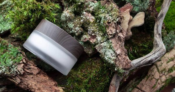 Natural cosmetic face or eye cream skincare frosted glass jar with wooden cup on forest background horizontal banner. Eco-friendly eco bio organic beauty product packing. Tree bark, branch and moss