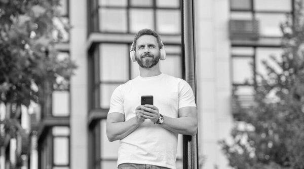 cheerful man choosing music playlist outside. photo of man choose music playlist on phone. man choose music playlist outdoor. man choose music playlist in the street.
