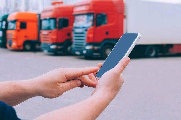 Mock up a smartphone in the hands of a man. Against the background of red trucks. Logistics concept