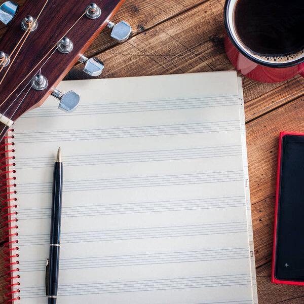 Clean sheet music notebook, guitar vulture, coffee and a smartphone on a wooden table, copy space, square