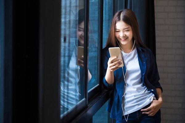 young happy woman standing at large window listening to music on