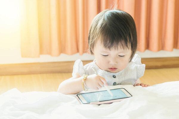 Infant, baby on a white bed, playing or learning drawing A B C using smart device pen on smart phone with blurred hand activity or movement concept