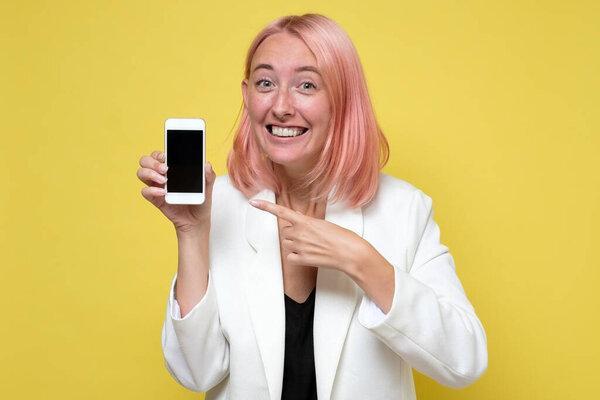 Smiling caucasian woman with dyed pink hair showing blank screen mobile phone