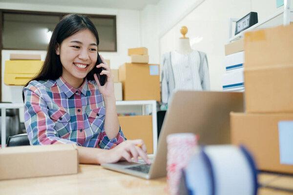 Young business startup online seller owner using computer for checking the customer orders from email or website and preparing packages for product office equipment.